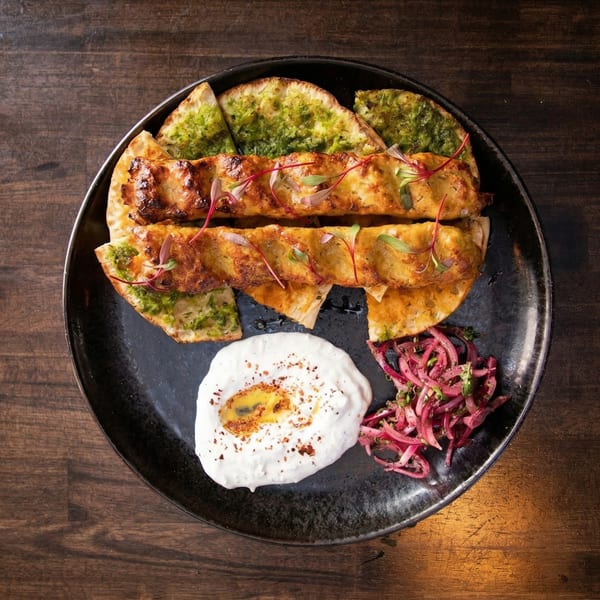 Two golden-brown chicken skewers on flatbread with green sauce, yogurt, and pickled red onions.