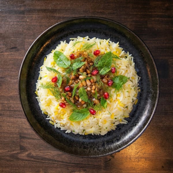 A black plate of yellow and white rice, topped with nuts, pomegranate seeds, mint, and dill.