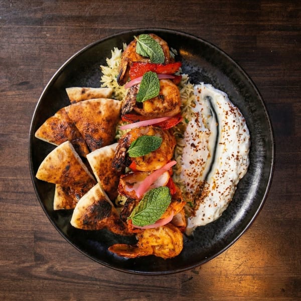 Grilled shrimp with rice, pita bread, red peppers, pickled onions, and a creamy sauce.