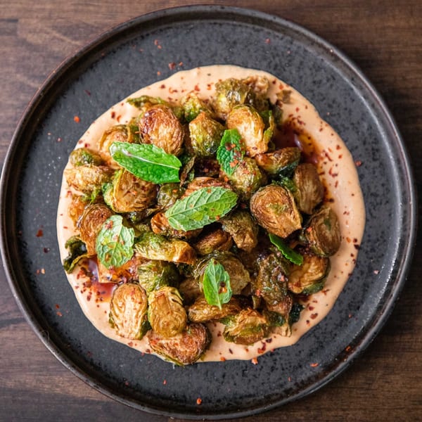 Crispy roasted Brussels sprouts with fresh mint and chili flakes on a creamy sauce, served on a dark plate.