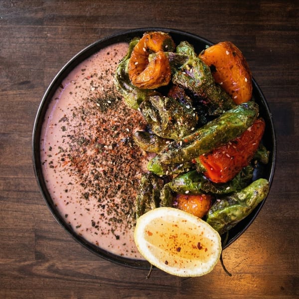 Roasted green and orange peppers with a lemon wedge, served on a pink sauce in a black bowl.