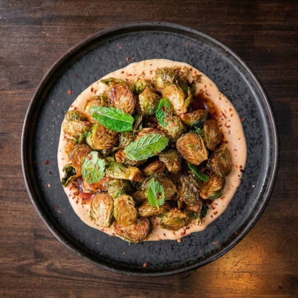 Roasted Brussels sprouts with sauce and mint leaves on a dark plate.
